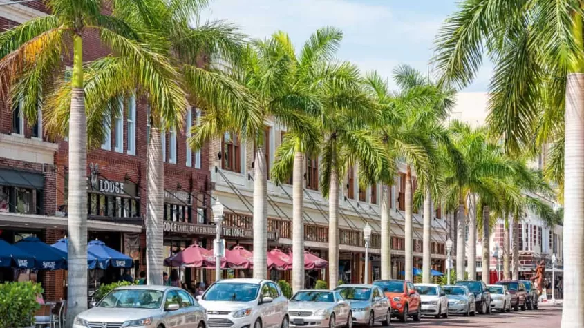 Picture of businesses, cars parked on first street and palm trees in downtown Fort Myers